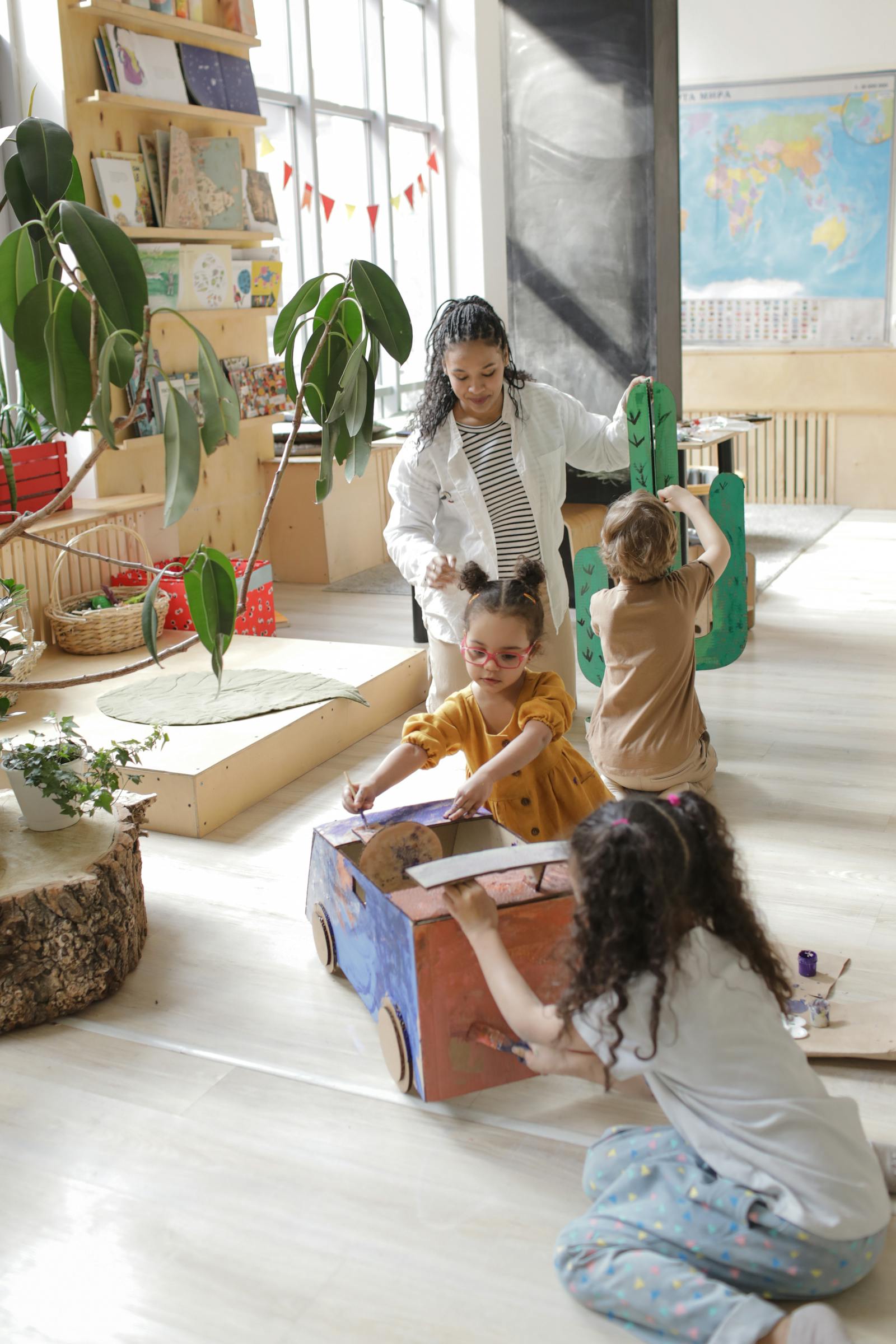 A caregiver at Alpha guiding young children through a bright, plant-filled playroom